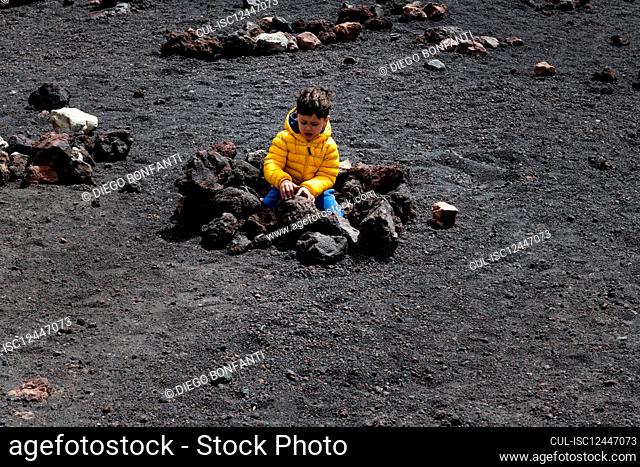 Italy, Sicily, Boy playing with rocks on Etna volcano