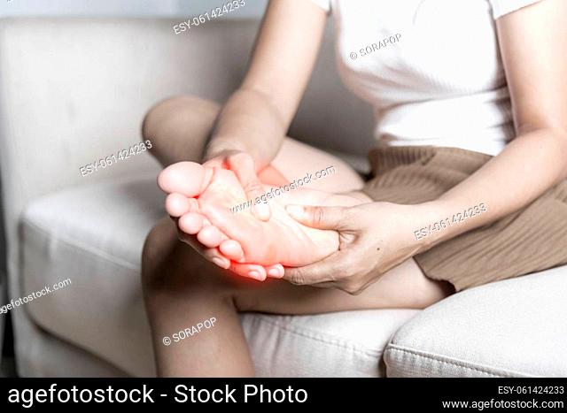 Foot pain, Asian woman sitting on sofa feeling pain in her foot at home, female suffering from feet ache use hand massage relax muscle from soles in home...