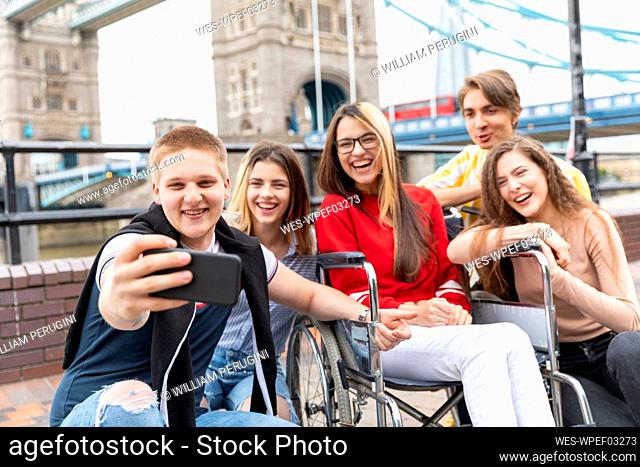 Happy young male and female friends taking selfie with Tower Bridge in background, London, UK