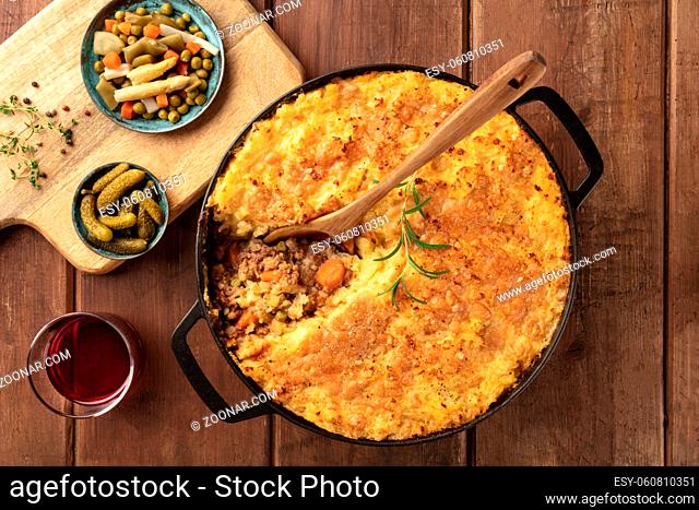 Shepherd's pie in a cooking pan with pickles, herbs, and red wine, overhead shot on a dark rustic wooden background