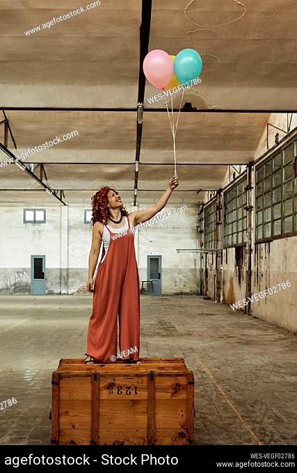 Woman standing on wooden box while holding colorful helium balloons