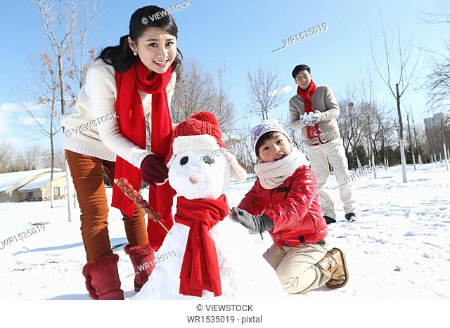 A family of three make a snowman in the outdoor