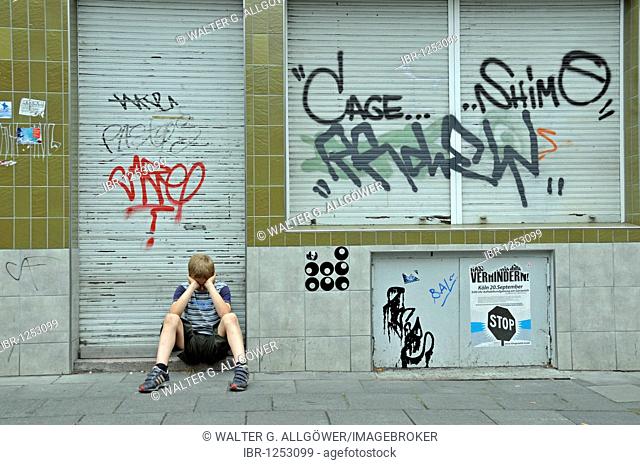 Lonely nine-year-old boy in front of a closed shop smeared with graffiti, Germany, Europe