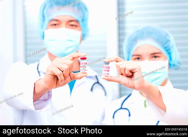 Young woman doctor or scientist in uniform wearing a face mask showing up coronavirus vaccine, nurse man holding bottle COVID-19 vaccination at laboratory