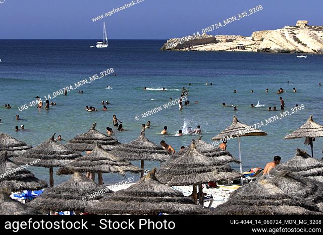 Thatched sunshades line Monastir Beach where holiday makers cool off in water Tunisia