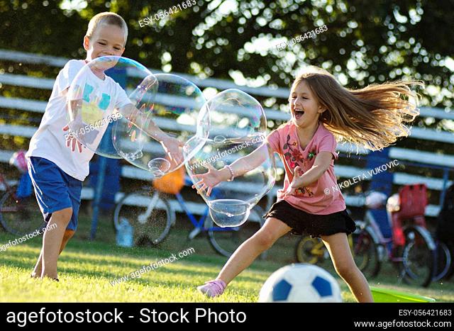 Playful happy children are playing with giant soap bubbles outdoors, cheerful childhood