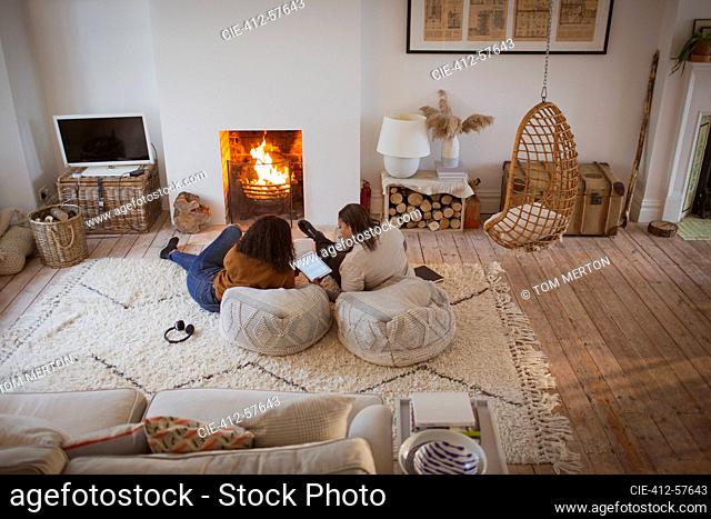 Mother and daughter relaxing with digital tablet by cozy fireplace