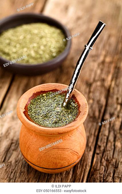 Traditional South American Yerba Mate tea in wooden mate cup with bombilla metal straw serving as a sieve, photographed on rustic wood (Selective Focus