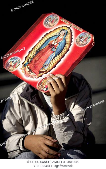 A pilgrim carrying an image of the Our Lady of Guadalupe covers his face from the sun outside of the Our Lady of Guadalupe Basilica in Mexico City, December 9