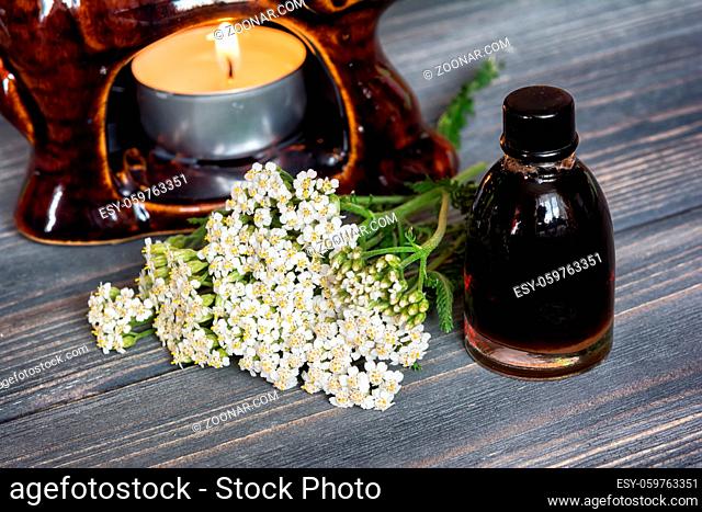 Essential yarrow oil and flower, candle on dark wooden background