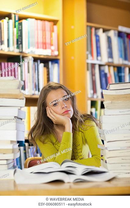 Tired beautiful student studying between piles of books