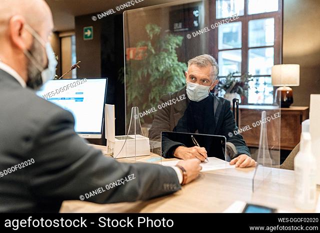 Man wearing protective face mask filling form at hotel reception