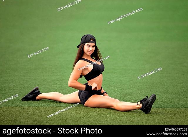 Athletic brunette woman shows a stretch on a green soccer field. Healthy lifestyle, sports