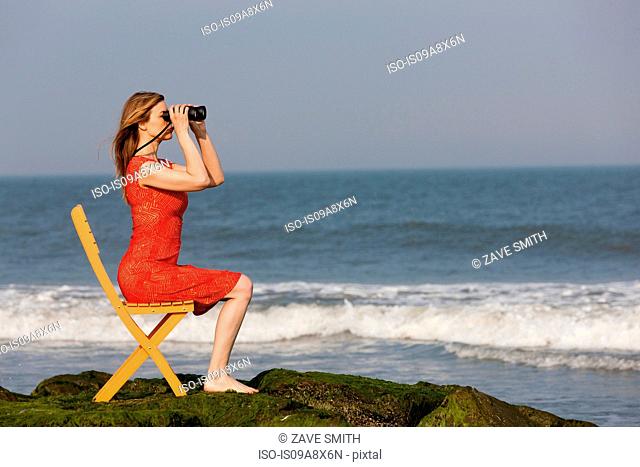 Mature woman sitting on chair on beach with binoculars