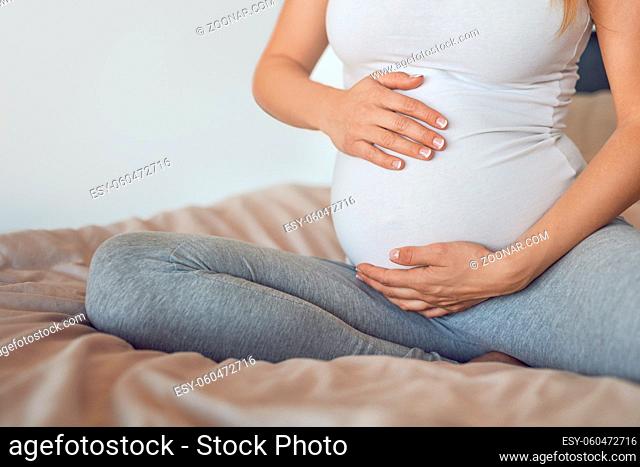 Young pregnant woman cradling her baby bump or belly with her hands in a close up cropped view conceptual of maternal love