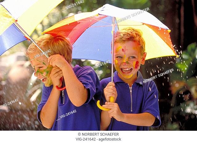 portrait, half-figure, two blond 5-year-old twin-boys with painted faces wearing blue t-shirts with multi-coulered umbrellas in their hands  - GERMANY