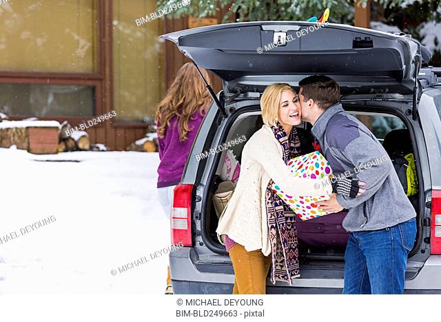 Caucasian man whispering to woman carrying gifts from car in winter
