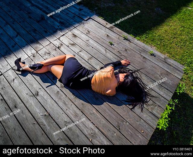Young woman lying down on wooden platform fanciful outfit clothing hidden identity legs heels
