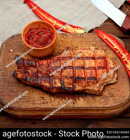 pork fried steak on the rib lies on a vintage brown wooden board, next to fresh red chili peppers, top view