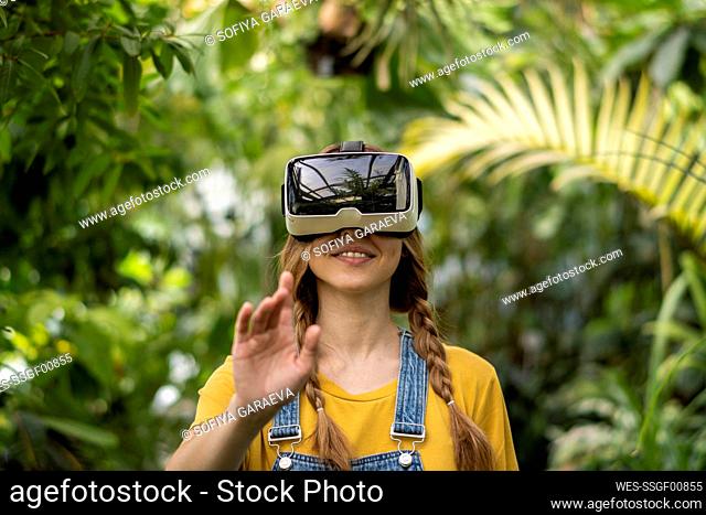 Smiling young woman wearing virtual reality simulator gesturing in garden