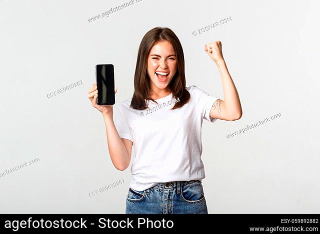Rejoicing beautiful girl showing smartphone screen and dancing like champion