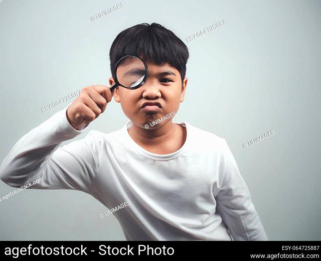 A boy wearing a white long-sleeved shirt is holding a magnifying glass on a white background