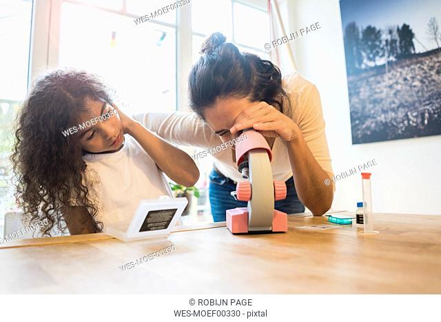 Mother helping daughter with homework, using microscope