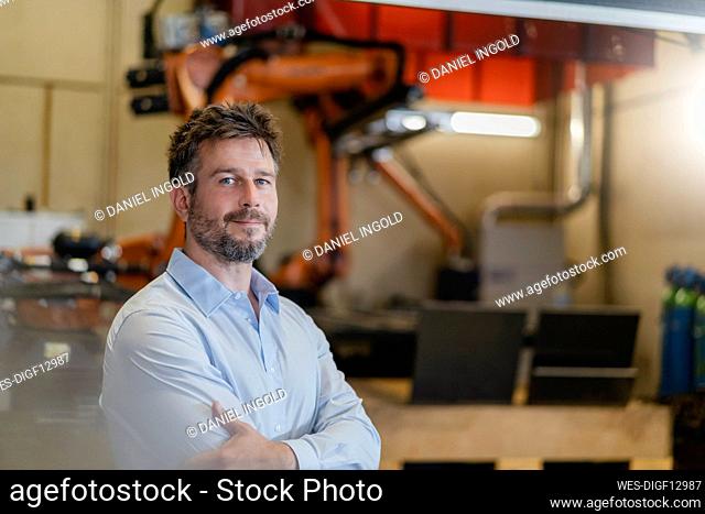 Confident businessman standing against automated robotic arm machine at factory