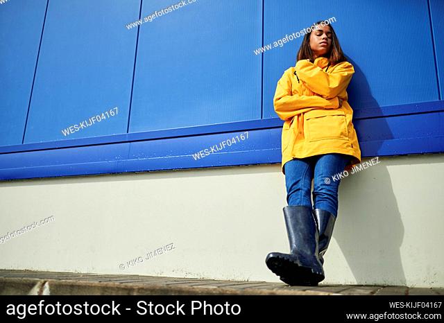 Woman with eyes closed leaning on blue wall during sunny day