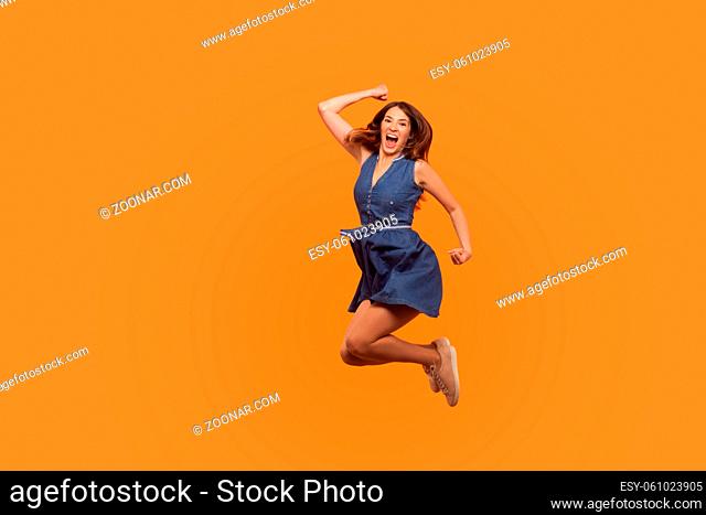Winner joy. Full length of energetic vivid brunette woman in denim dress flying in air with inspired ecstatic expression, celebrating great success