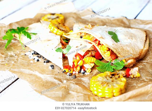 Mexican Quesadilla wrap with vegetables, corn, sweet pepper and sauces on the parchment and table. horizontal view
