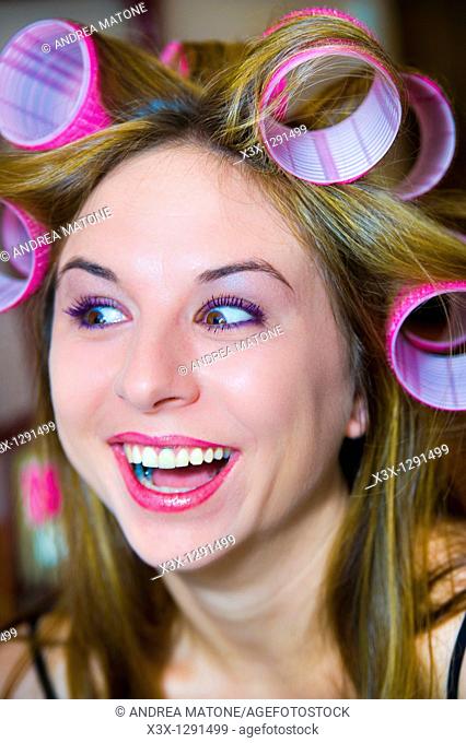 Woman with curlers in her hair smiling in surprise after make up session