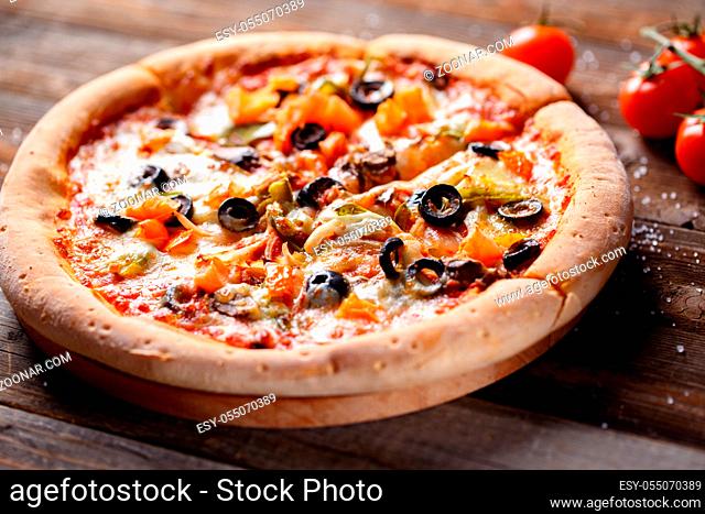 Pizza with tomato, mushroom and olives on wooden table with tomatos, fresh onion on background