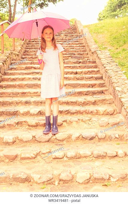 Child girl with umbrella stands on the stairs