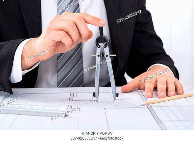Close-up Of Young Male Architect Hands Holding Compass On Blueprint At Desk In Office