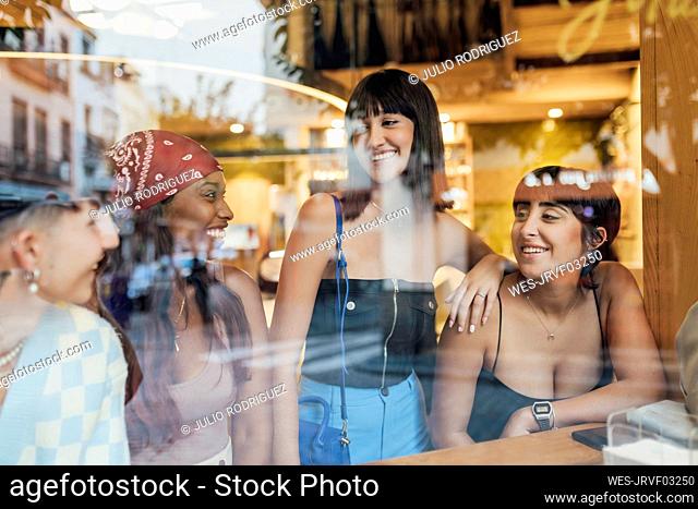 Happy multiracial friends enjoying in cafe seen through glass