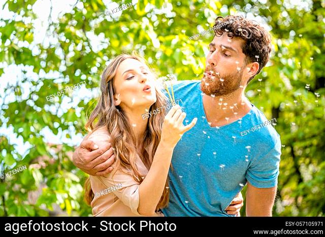 Young couple daydreaming about their future blowing dandelion seeds being visibly happy