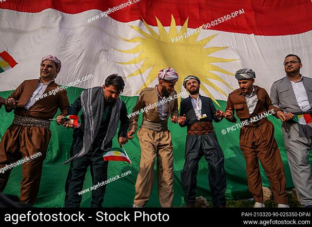 20 March 2021, Iraq, Akre: Kurdish men dance, backdropped by a giant Kurdish flag, during the celebrations of Nowruz, the Persian new year