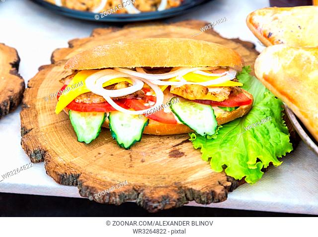 Burger with chicken meat, cheese and fresh vegetables on wooden board. Simple idea for vegetarian sandwich