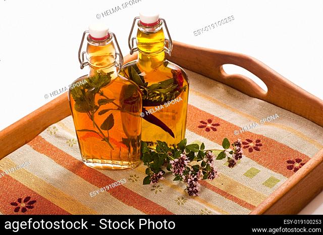 Flaschen mit Essig und Öl auf Holztablett mit eingelegten Kräute