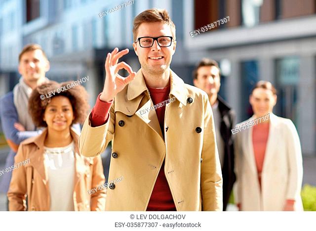 business, gesture and corporate concept - happy smiling man with international group of people showing ok hand sign outdoors