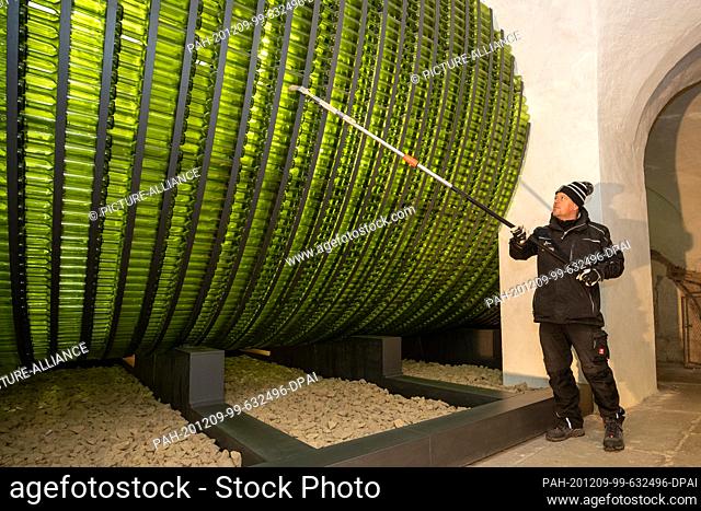 04 December 2020, Saxony, Königstein: Jens Hickmann cleans with a brush and an extension from the outside over the wine bottles