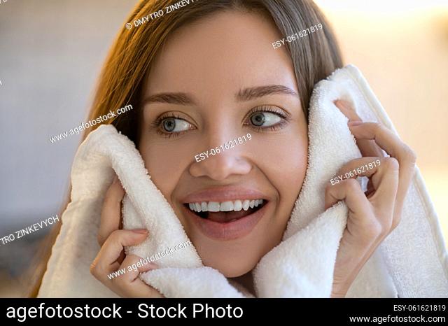Pleasure. Close up of hands with towel touching face of young beautiful joyful caucasian woman looking away