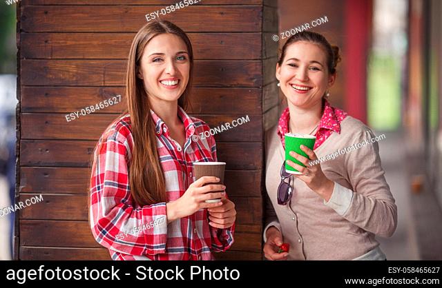 Toned picture of best friends smiling or laughing while holding cups of coffee near cafe or restaurant