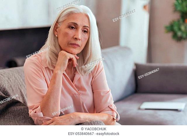 First sign of depression. Waist up of a thoughtful aged woman sitting on the couch and thinking about her life while feeling sad