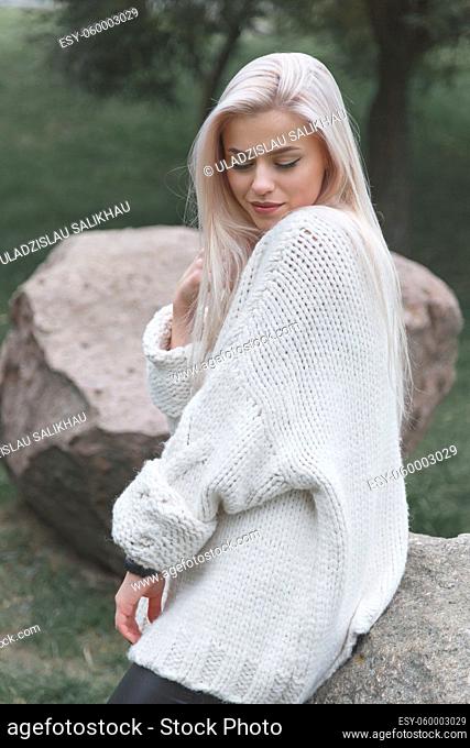Young blonde female wearing knitted white sweater. Women fashion concept
