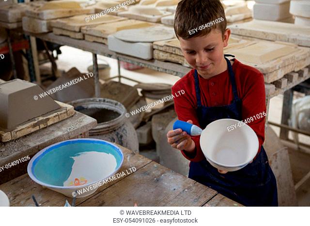 Boy decorating bowl with water color in pottery workshop