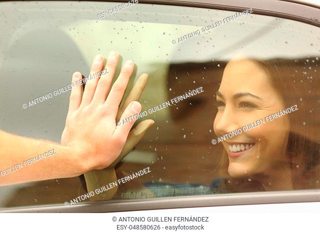 Happy couple or friends saying good bye touching hands through a car window before travel