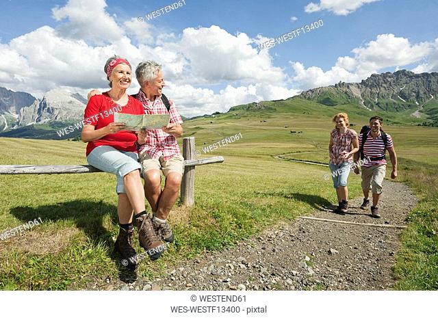 Italy, Seiseralm, Senior couple holding map, couple hiking in background