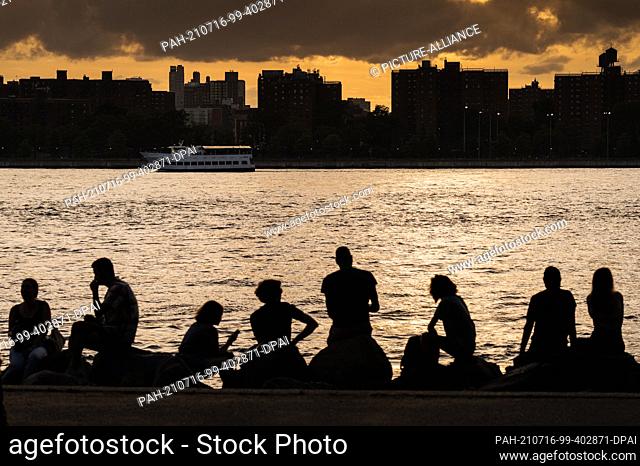 PRODUCTION - 26 June 2021, US, New York: People enjoy the day at sunset on the East River in Brooklyn. New York is well on its way to making up for its forced...